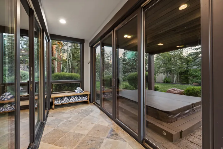Enclosed patio with full-height sliding glass doors and transom windows, featuring stone tile flooring and recessed ceiling lighting
