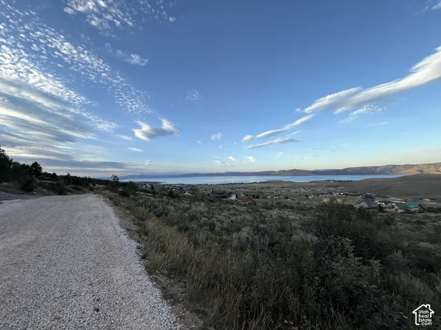 Elevated land parcel featuring a gravel access road, native vegetation, and a wide-reaching vista of the lake and distant mountains