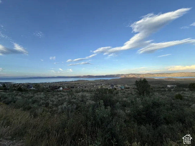 Expansive landscape featuring rolling hills, native shrubbery, and open water, set against a backdrop of distant mountains
