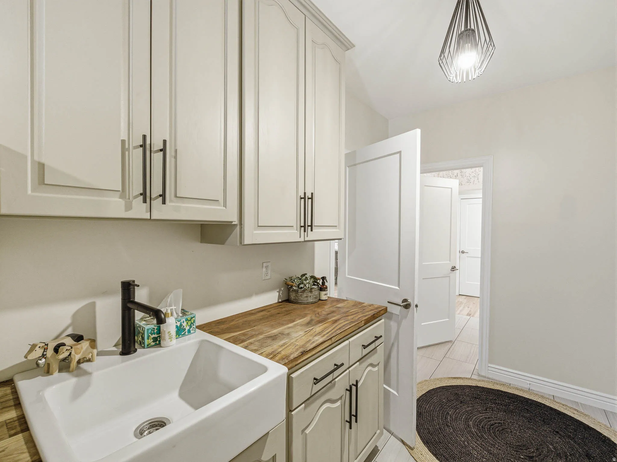 Utility room featuring light-toned cabinetry, wood-finish countertop, and a white farmhouse-style sink with a matte black faucet