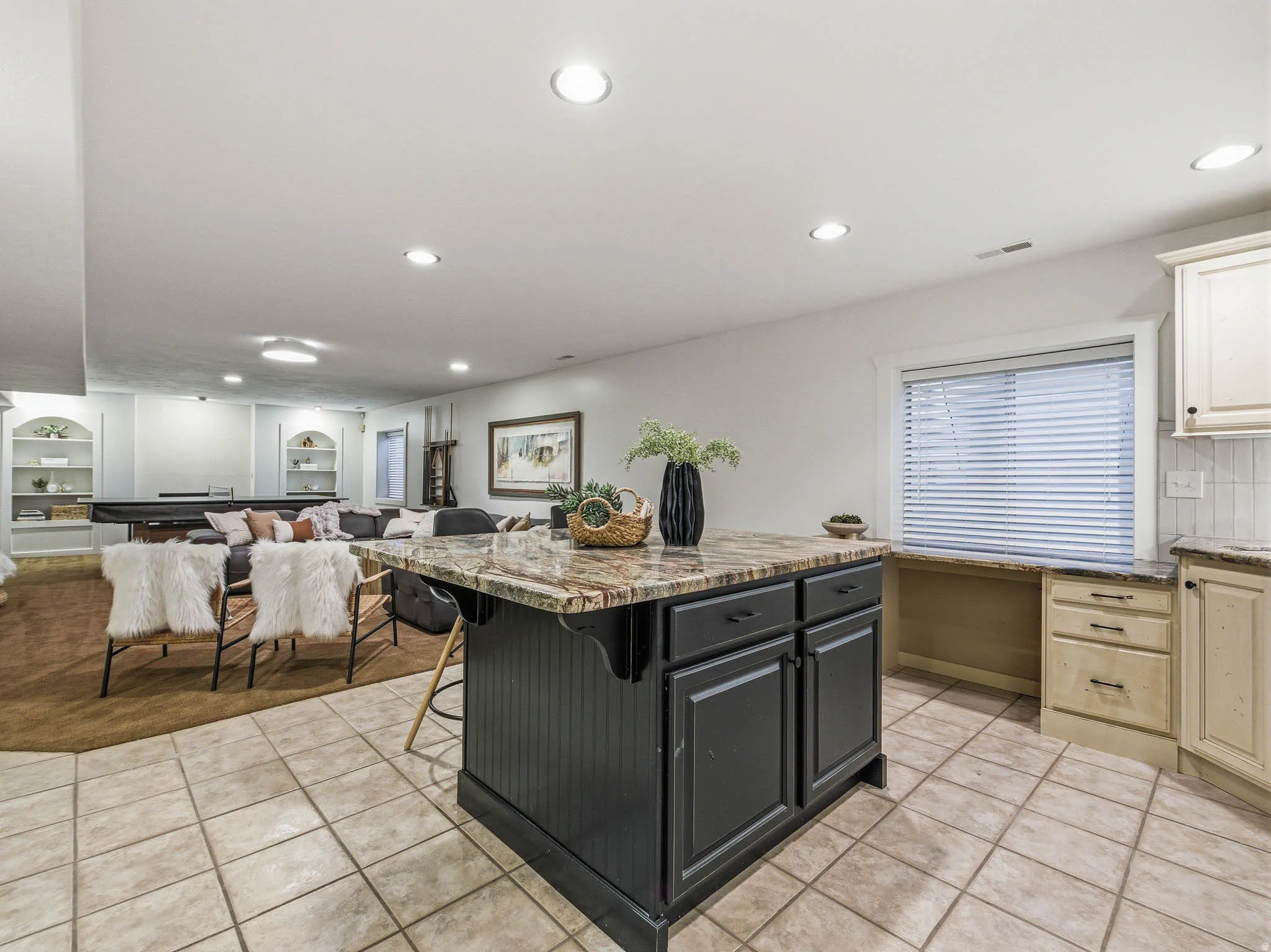 Kitchenette featuring a black island with a stone-finish countertop, tiled flooring, built-in cabinetry, and a window with blinds
