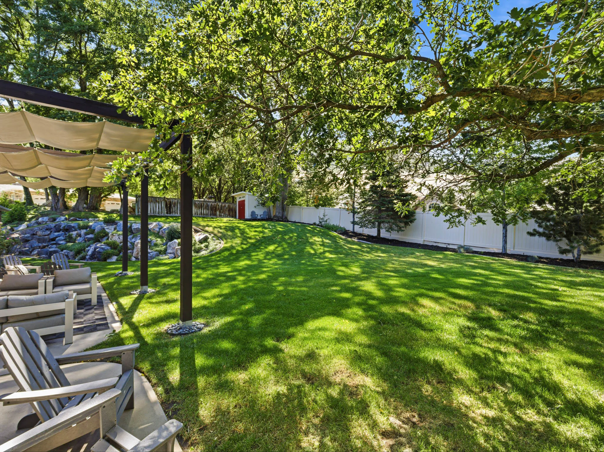 Expansive backyard featuring a lush lawn, mature trees, and a white privacy fence