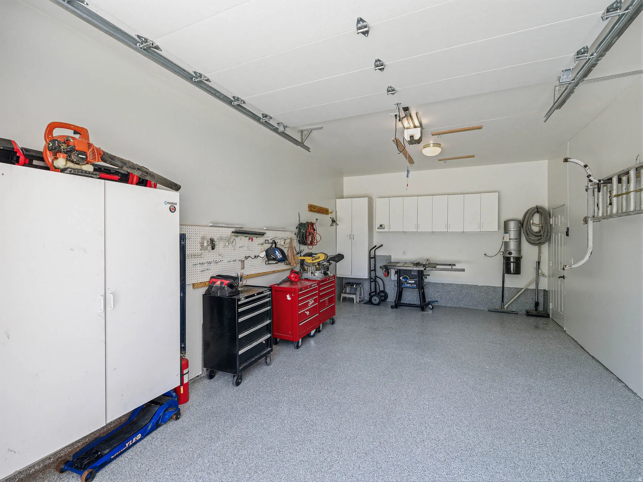 Spacious garage featuring a durable epoxy floor, integrated wall-mounted cabinetry, built-in shelving, overhead lighting, and white finished walls