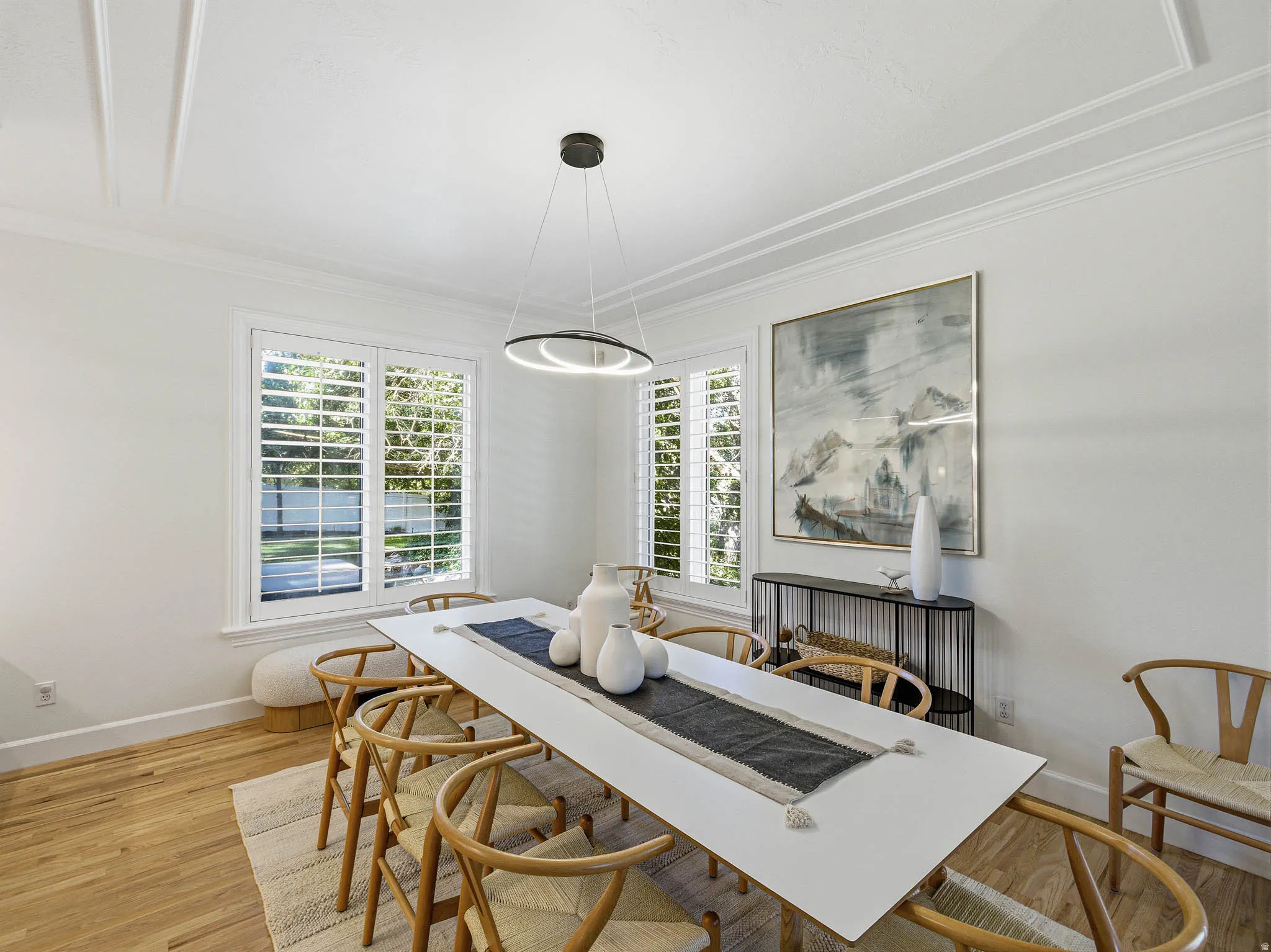 Dining area featuring hardwood flooring, white plantation shutters, an overhead modern ring chandelier, and detailed ceiling trim work