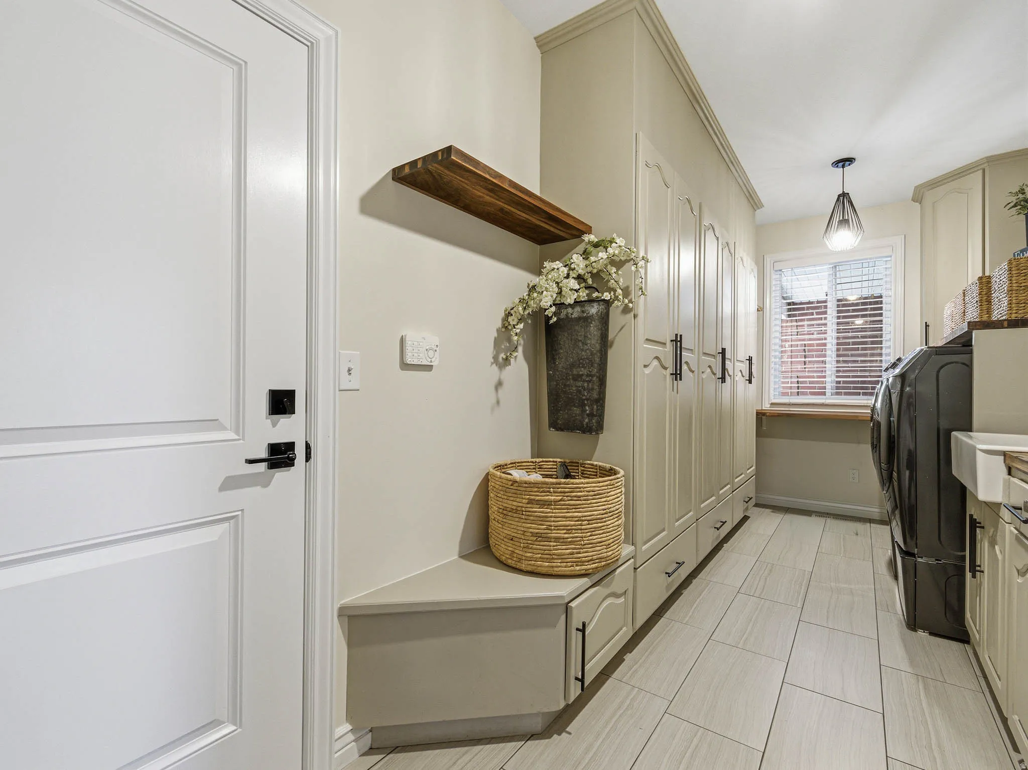 Functional utility room featuring extensive built-in cabinetry with black hardware, plank-style flooring, a transom window with blinds, a built-in bench, and a floating wood shelf