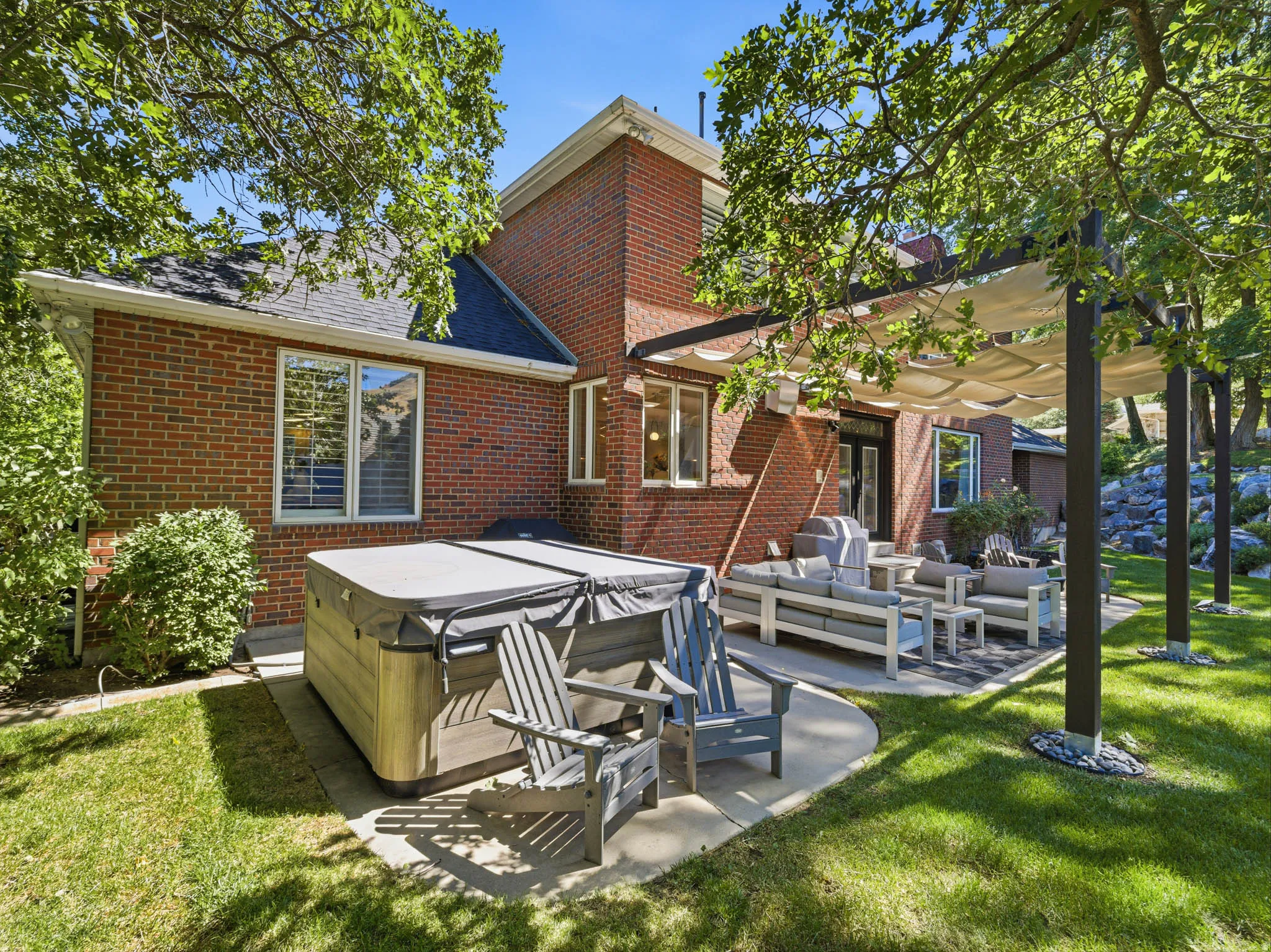 Brick exterior featuring a covered patio, hot tub, and mature landscaping