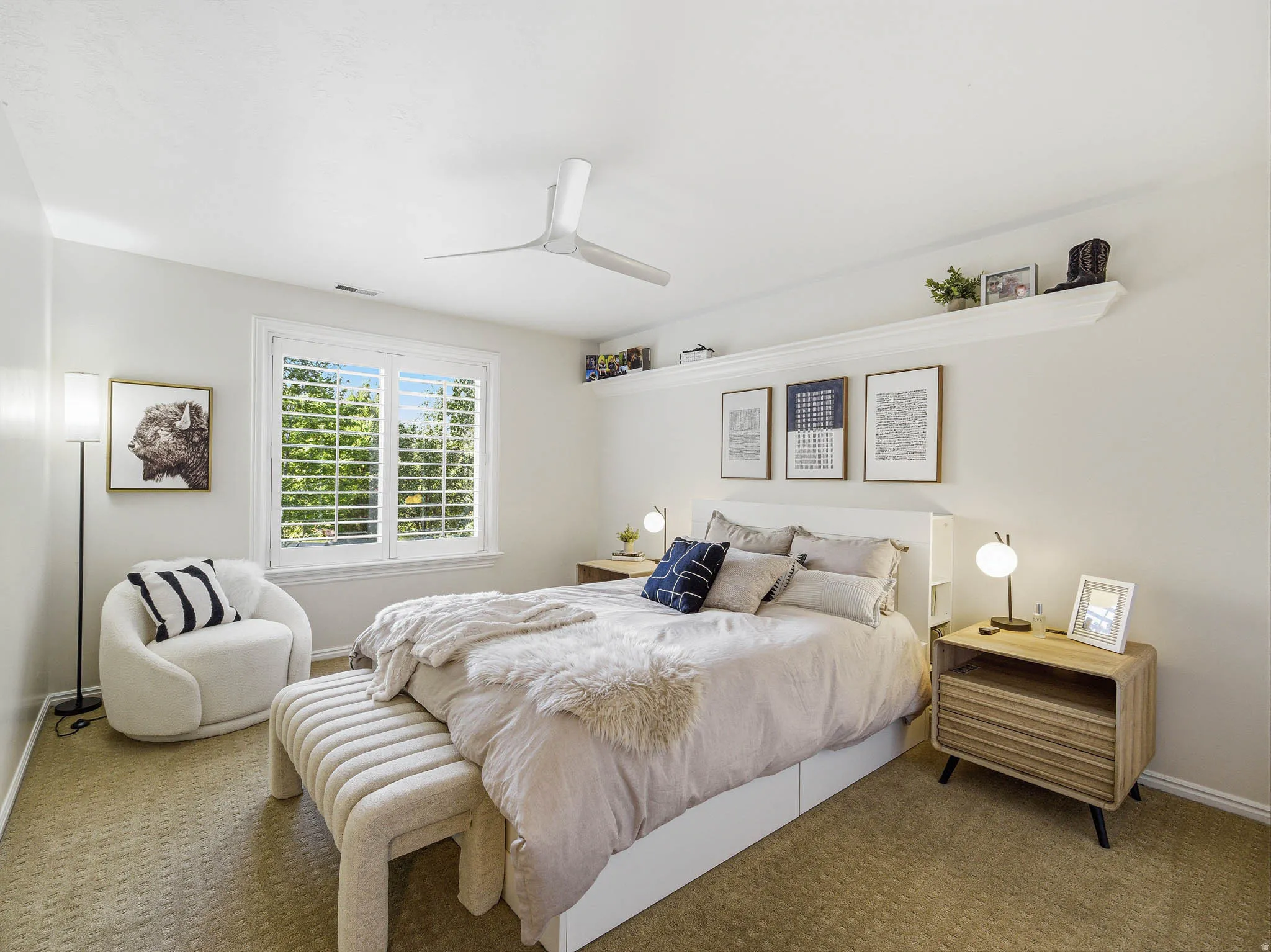 Bright bedroom featuring a large window with plantation shutters, a contemporary ceiling fan, and carpeted flooring