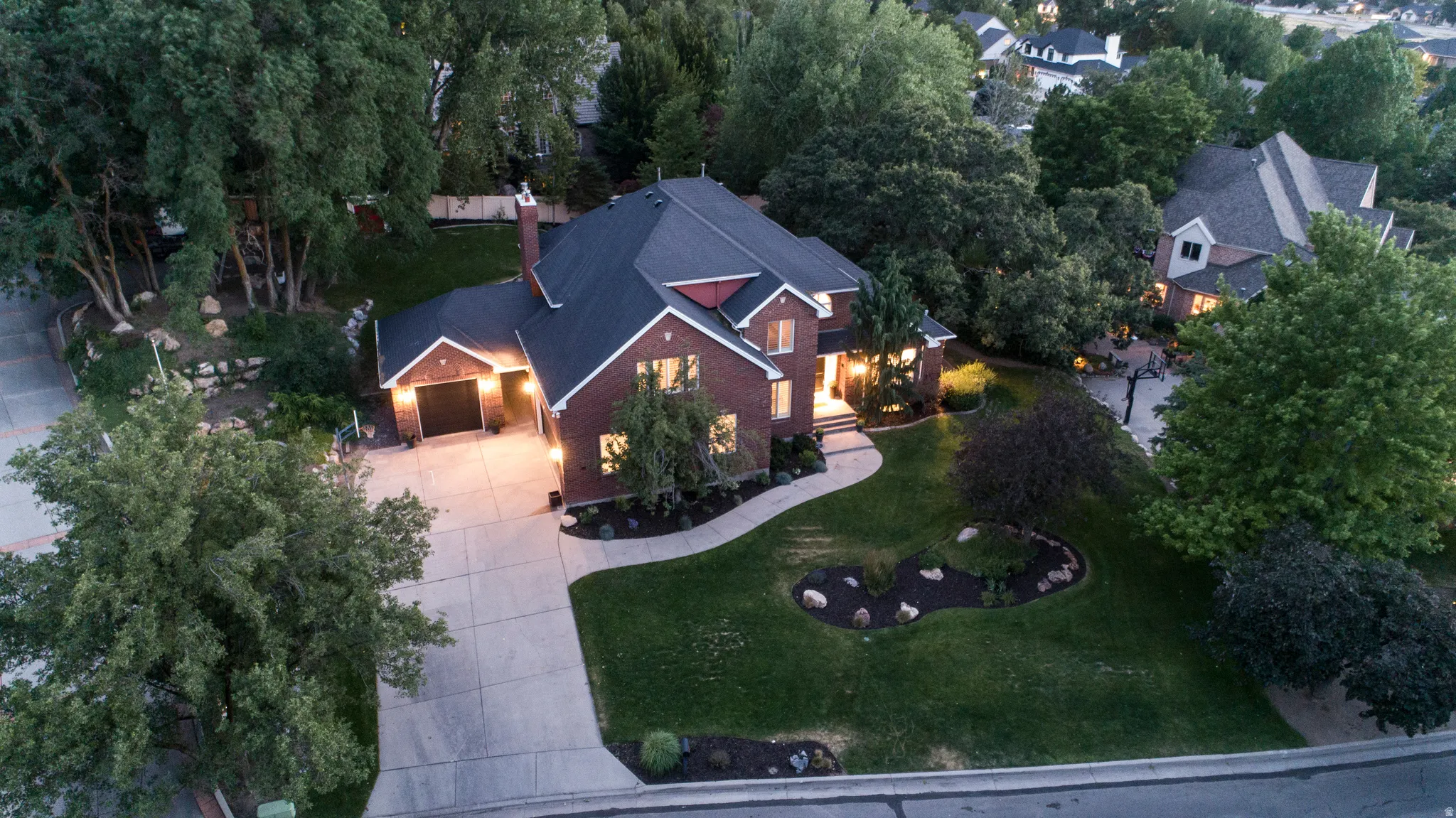 Brick exterior residence featuring a dark shingled roof, an attached garage, a concrete driveway, and mature landscaping with established trees and a manicured lawn