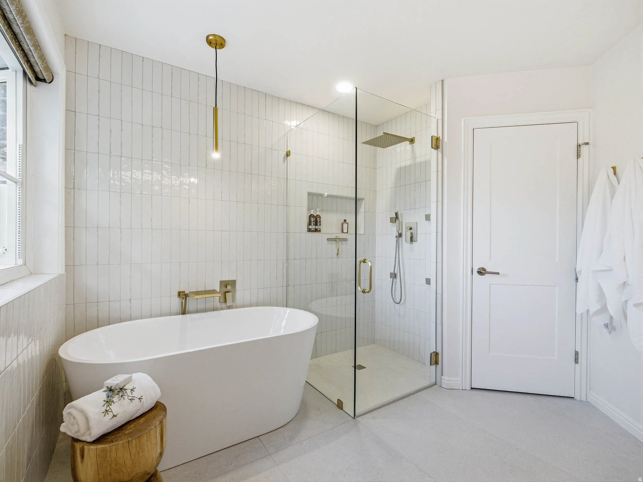 Freestanding soaking tub with a wall-mounted brass faucet, glass-enclosed shower with a rainfall showerhead, and vertical subway tile accents