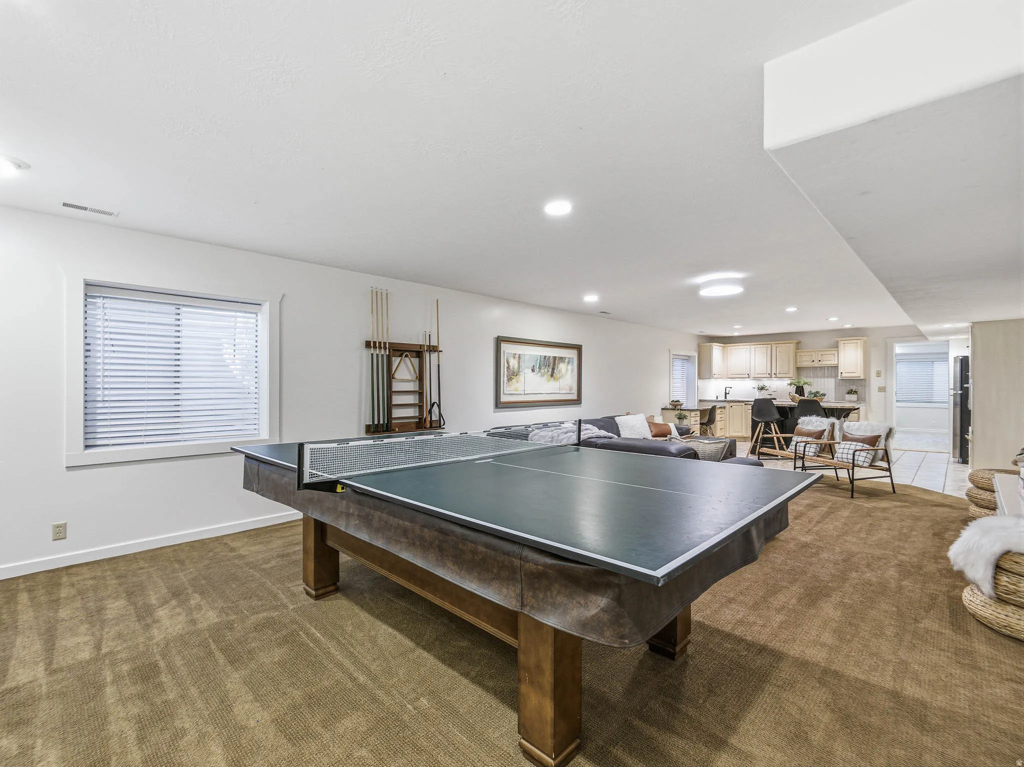 Expansive recreation room featuring a large window with blinds, recessed lighting, and a neutral carpeted floor