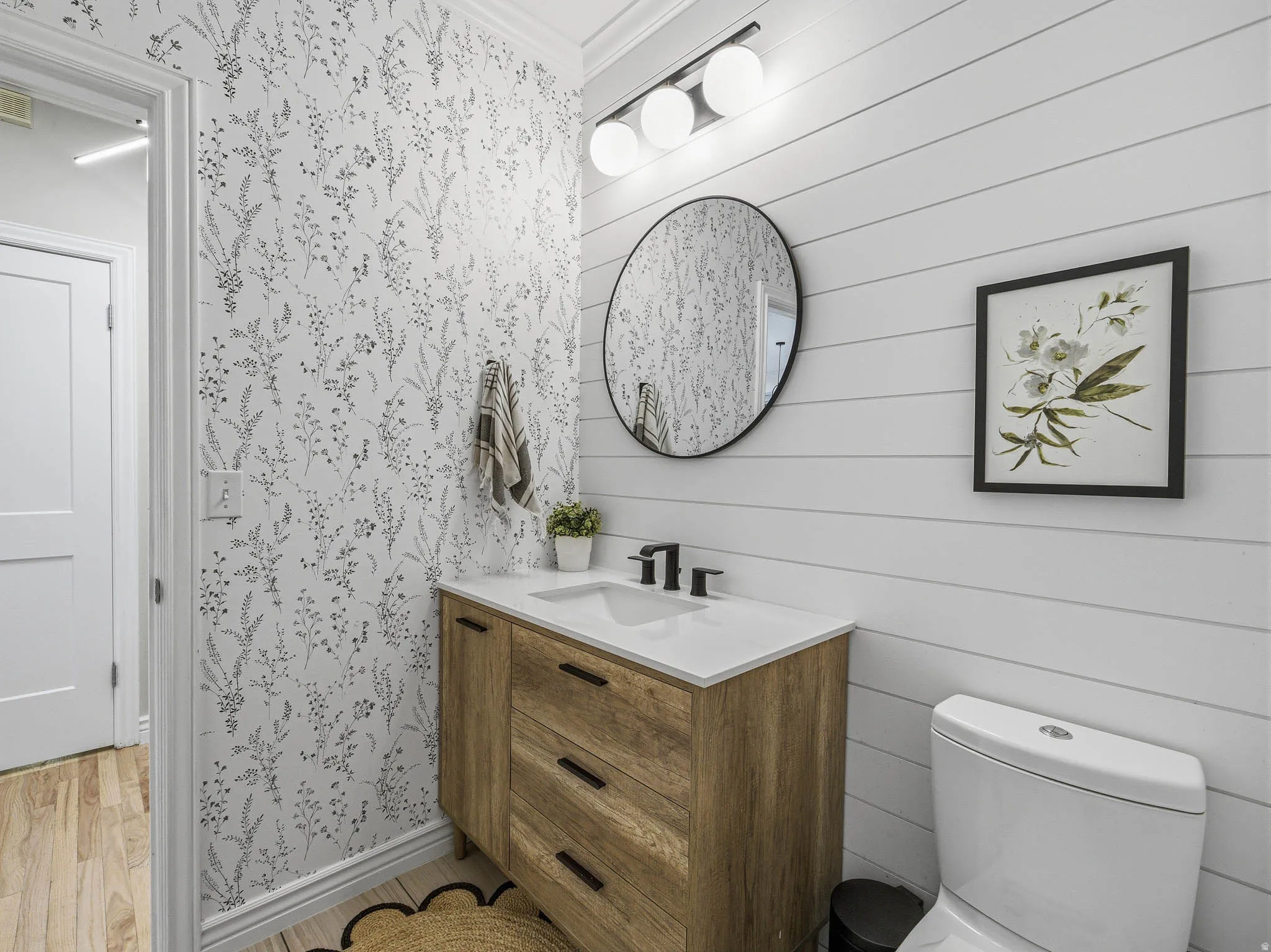 Powder room featuring shiplap wall paneling, a wood-finish vanity with an integrated sink, and black hardware
