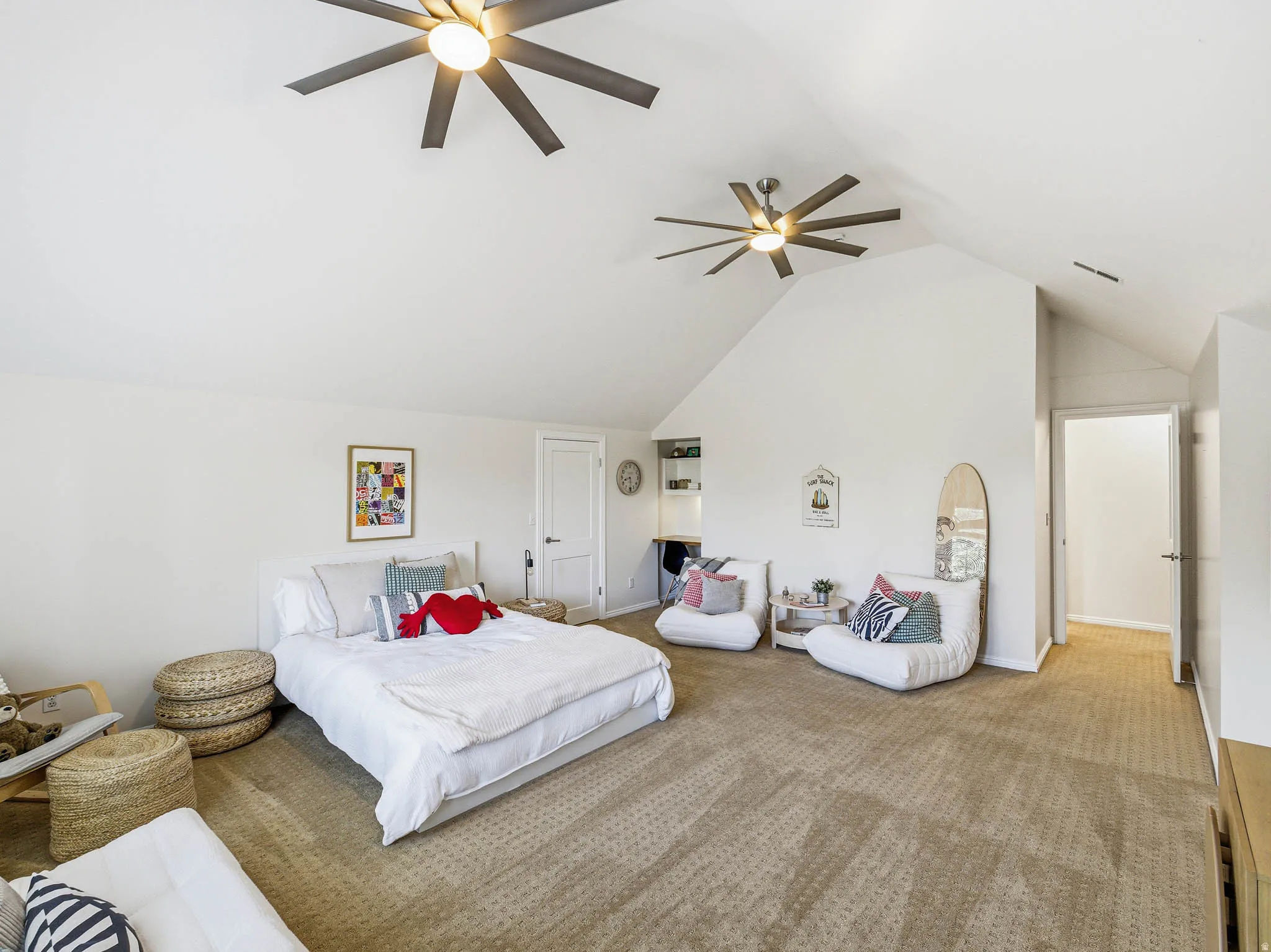 Spacious room featuring vaulted ceilings, two contemporary ceiling fans, light-toned carpeting, and a built-in desk with shelving