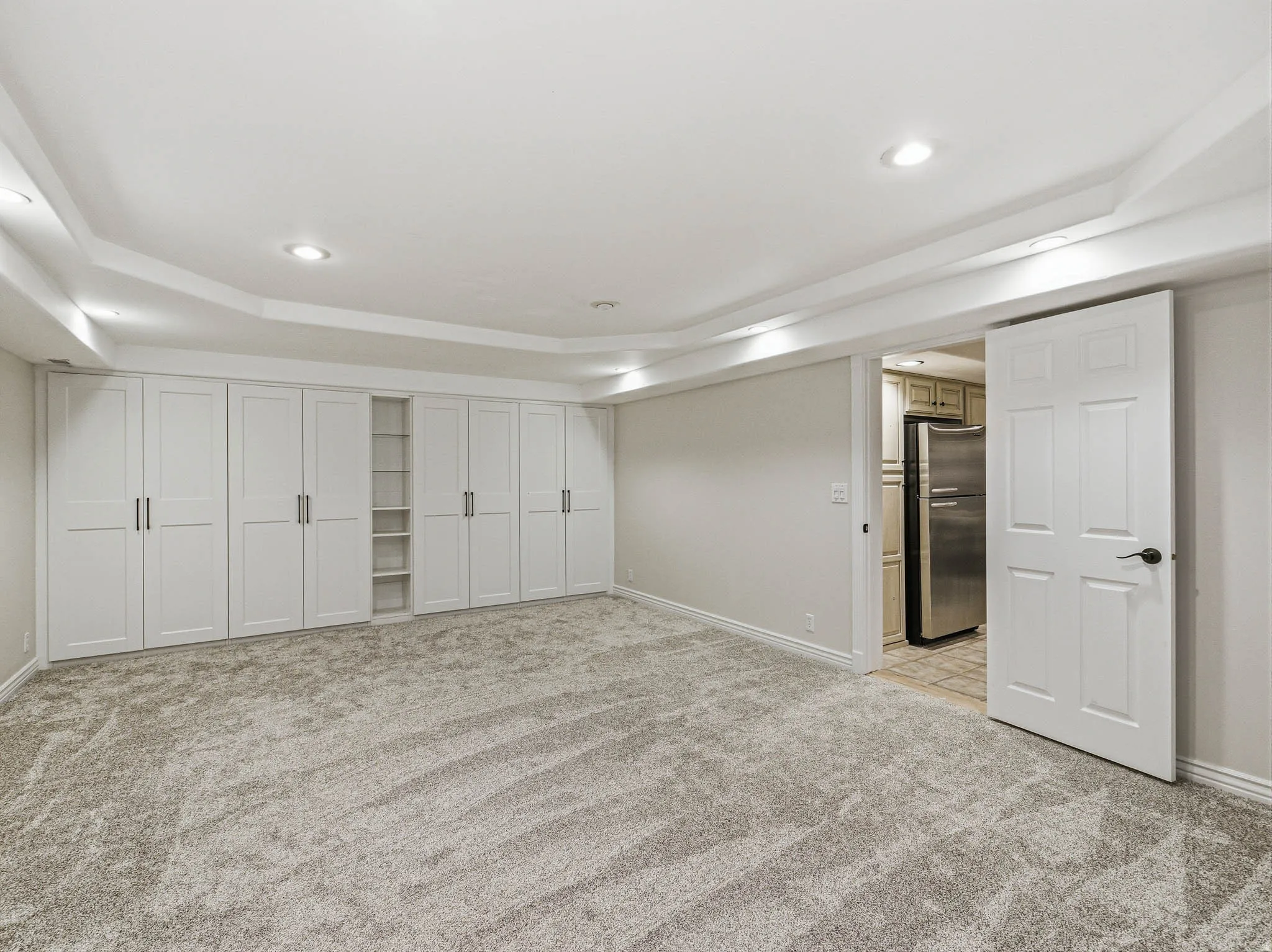 Spacious room featuring extensive built-in white cabinetry with black hardware, recessed lighting, and grey patterned carpeting