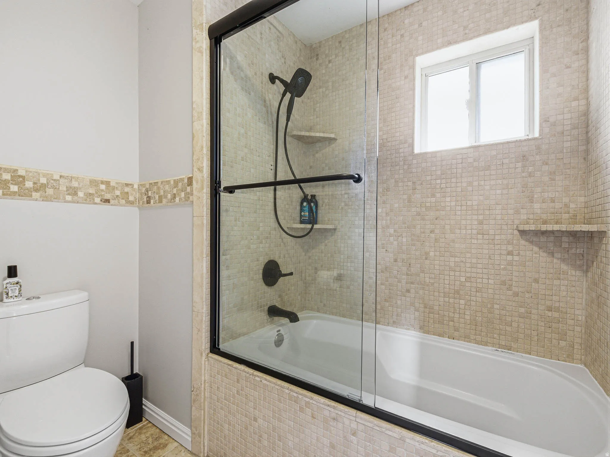 Tub and shower combination featuring a glass enclosure with matte black trim, mosaic tile surround, and built-in shelving