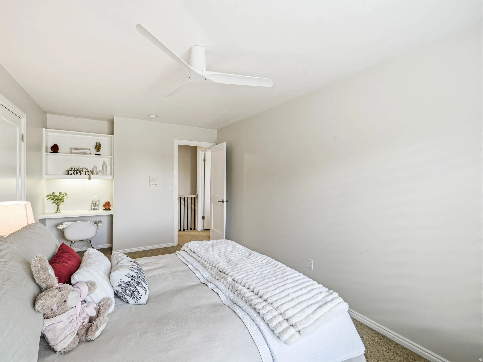 Bedroom featuring neutral-toned walls, built-in shelving, integrated desk space with task lighting, and a modern ceiling fan