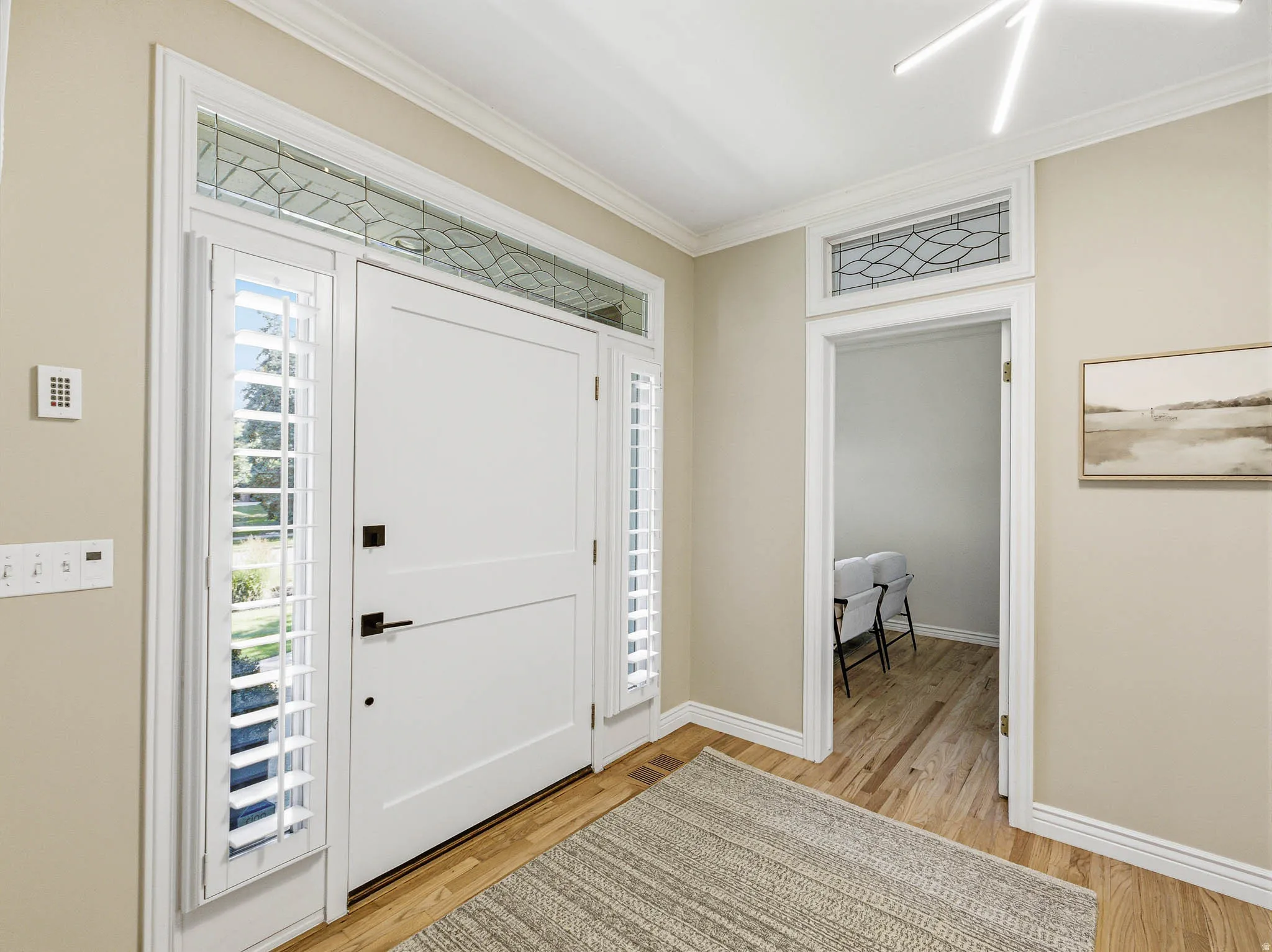 Entryway featuring a white paneled front door with matte black hardware, sidelight windows with plantation shutters, and a decorative transom window