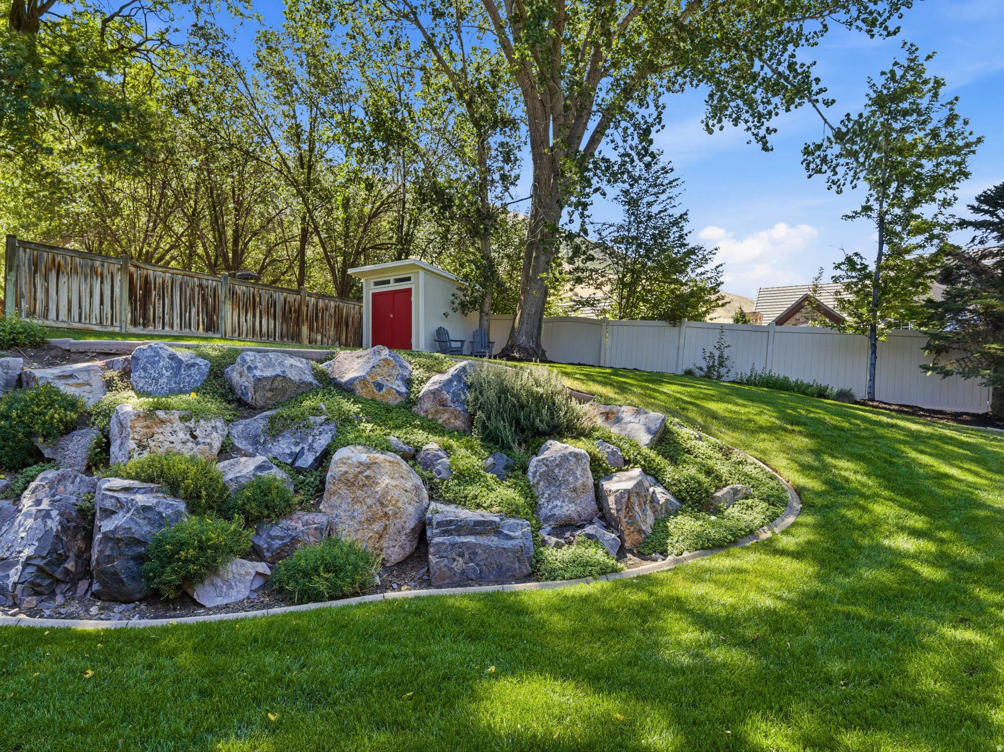 Expansive green lawn with a rock garden and mature trees