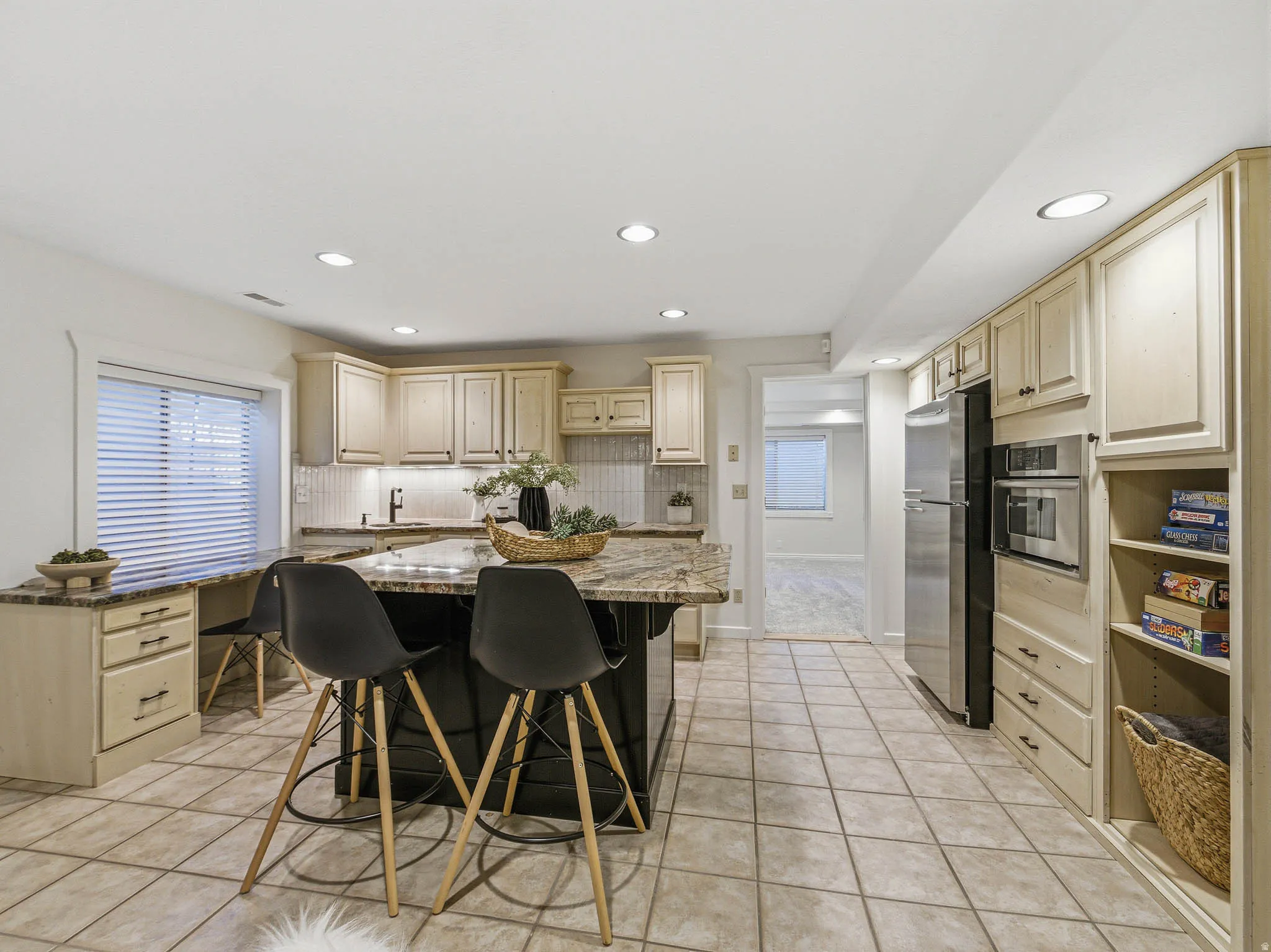 Kitchen featuring a multi-tone island with a granite-style countertop, integrated stainless steel appliances, light wood-finish cabinetry, tile flooring, and recessed ceiling lighting
