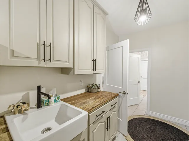Utility room featuring light-toned cabinetry, wood-finish countertop, and a white farmhouse-style sink with a matte black faucet