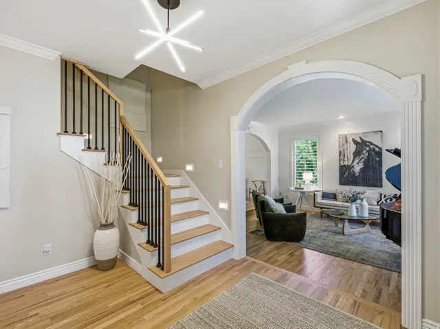 Hardwood flooring throughout the entry, staircase with wood treads, black balusters, and a light wood handrail