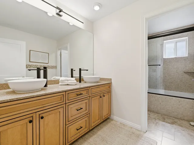 Double vanity with vessel sinks, black fixtures, granite-finish countertop, and wood cabinetry