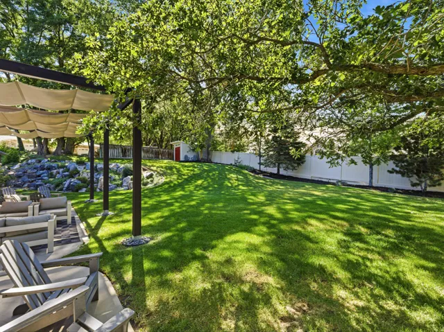 Expansive backyard featuring a lush lawn, mature trees, and a white privacy fence