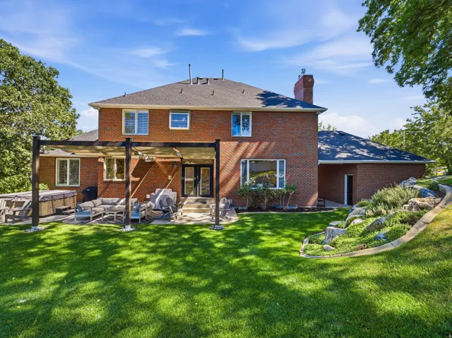 Brick exterior residence featuring a covered patio, expansive lawn, and tiered rock landscaping