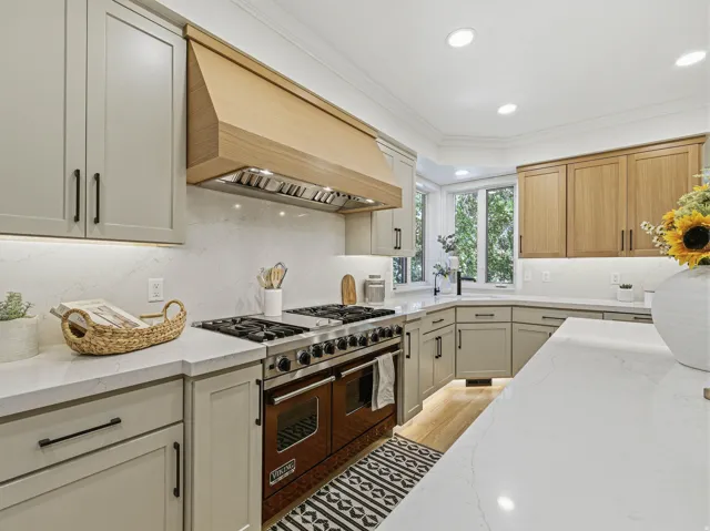 Gourmet kitchen featuring a professional-grade range, custom wood range hood, light-toned cabinetry, quartz countertops, and a bay window