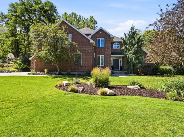 Brick exterior residence featuring a front entry with sidelights, a landscaped front yard with mature trees, and an arched window accent
