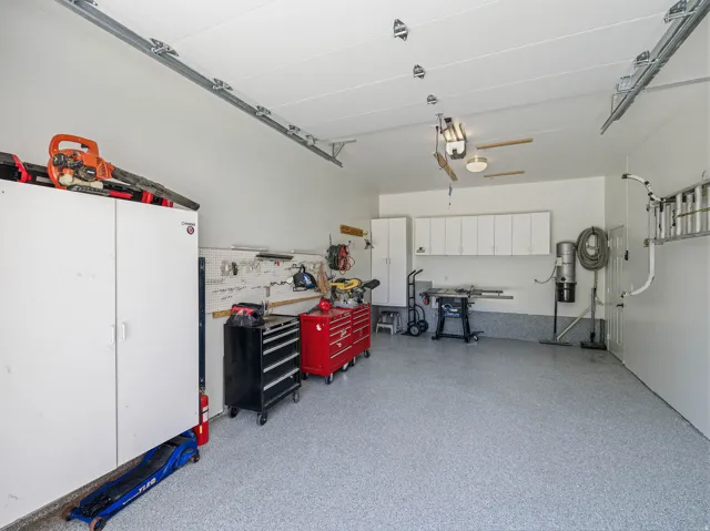 Spacious garage featuring a durable epoxy floor, integrated wall-mounted cabinetry, built-in shelving, overhead lighting, and white finished walls