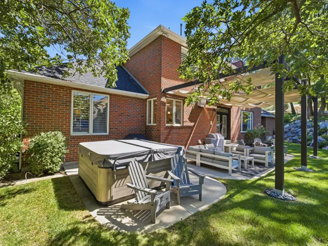Brick exterior featuring a covered patio, hot tub, and mature landscaping