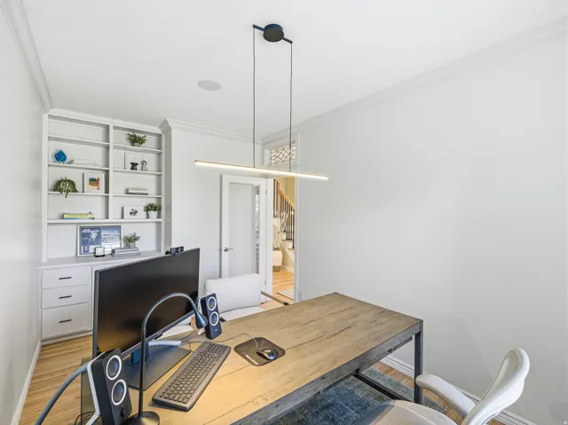 Office space featuring built-in shelving, integrated cabinetry with dark hardware, crown molding, and wood-finish flooring