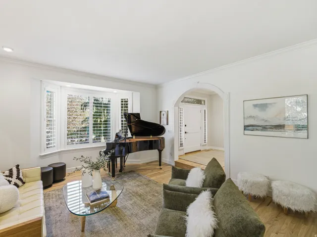 Living area featuring a bay window with plantation shutters, recessed lighting, crown molding, and wood-finish flooring