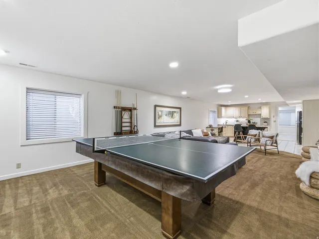 Expansive recreation room featuring a large window with blinds, recessed lighting, and a neutral carpeted floor
