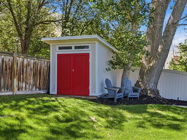Storage shed with vibrant red double doors and transom windows, accompanied by a manicured lawn and mature trees