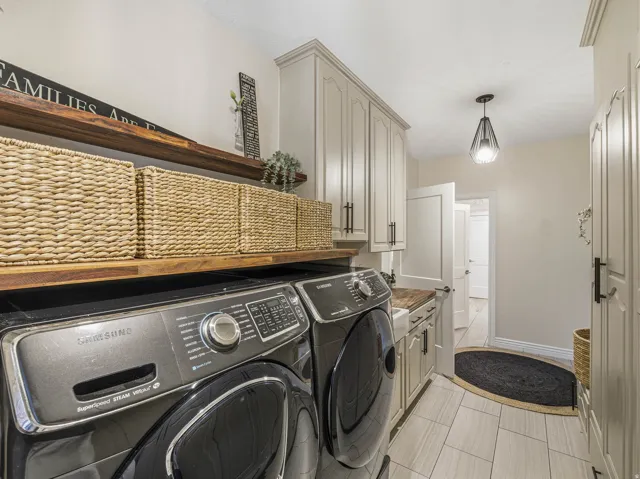Dedicated laundry area featuring light-toned cabinetry with dark hardware, wood-finish countertops, and matching floating shelves