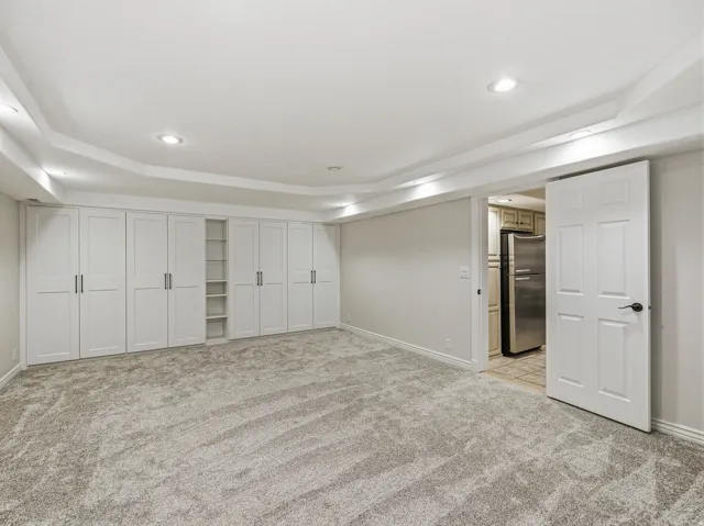 Spacious room featuring extensive built-in white cabinetry with black hardware, recessed lighting, and grey patterned carpeting