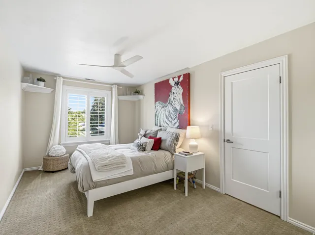 Neutral tone bedroom featuring patterned carpeting and a window with plantation shutters