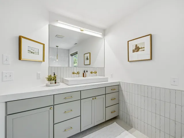 Contemporary vanity featuring a rectangular vessel sink, brass-finish wall-mounted faucet, and light gray cabinetry with brass-finish hardware