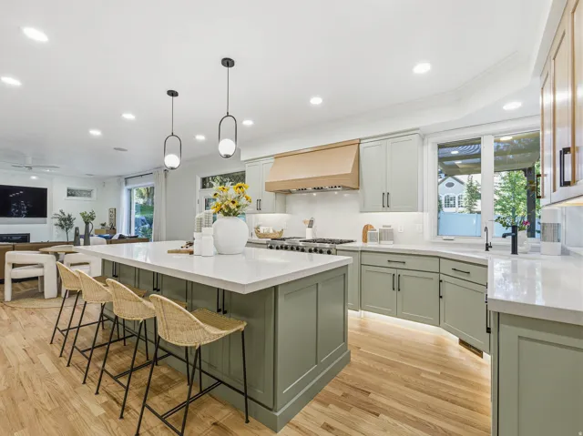 Gourmet kitchen featuring a large island with seating, light green cabinetry, white countertops, wood-finish flooring, and recessed lighting
