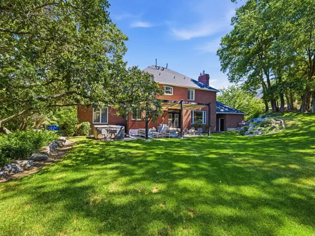 Spacious backyard with mature trees, a red brick exterior, a stone patio with a pergola, and a terraced rock garden