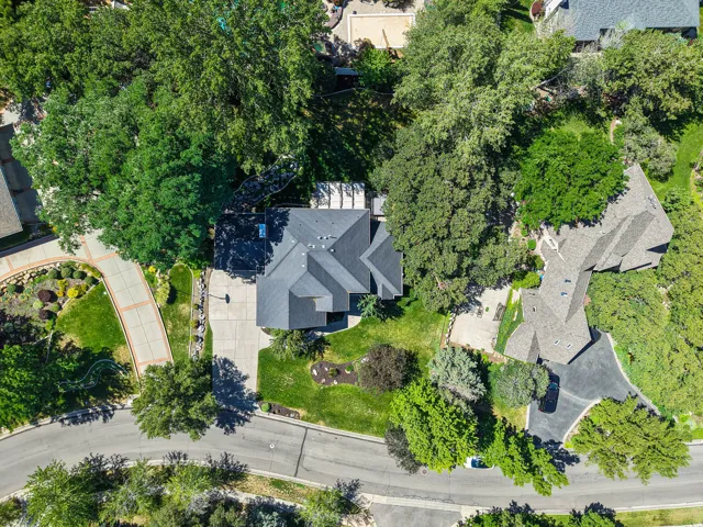 Aerial view showcasing a property with a multi-gabled roofline, extensive paved driveway, mature trees, and landscaping