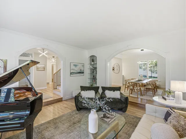 Expansive living area with wood-finish flooring, featuring arched doorways, built-in shelving, crown molding, and a dining area beyond