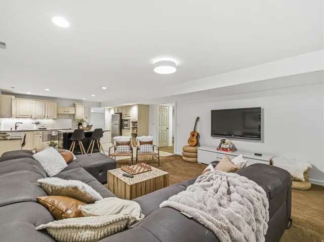 Open-concept living space featuring a full kitchen with light wood cabinetry, a dark island with seating, recessed lighting, and wall-mounted television