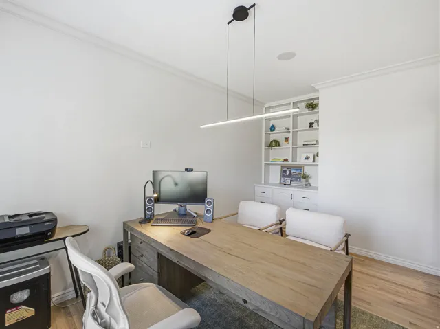 Dedicated workspace featuring built-in shelving, integrated lower cabinetry, a linear pendant light fixture, ceiling-mounted audio speaker, and hardwood flooring