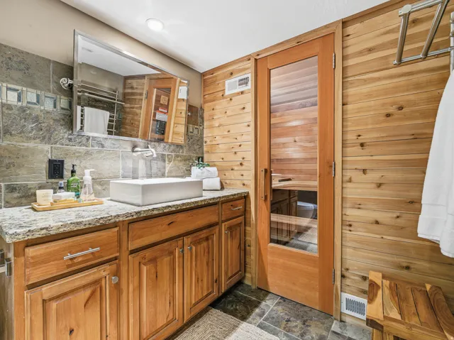 Bathroom featuring a wood-panel accent wall and a built-in sauna with a glass-paneled wooden door