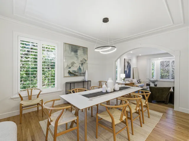 Dining space featuring wood-finish flooring, white plantation shutters, and a modern linear chandelier
