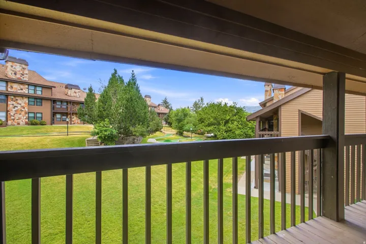 Wood-finish balcony with dark railings overlooking a manicured lawn area with mature trees