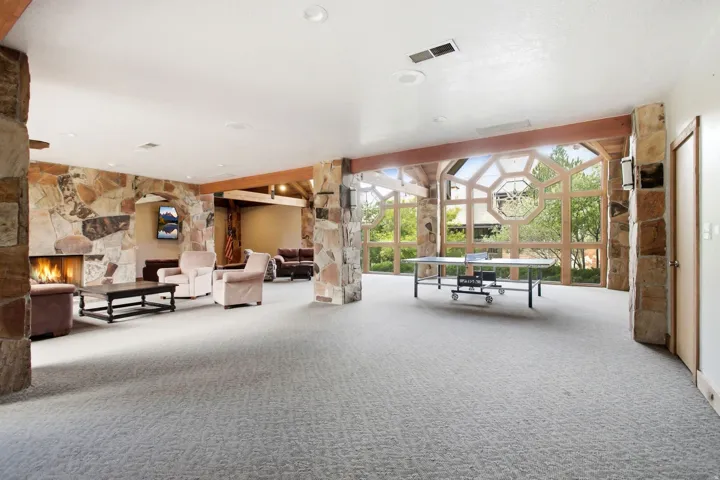 Spacious entertainment area featuring geometric window architecture, stone accent walls, exposed wood beams, recessed lighting, and soft carpet flooring