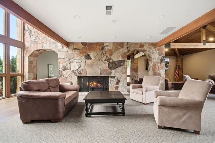 Spacious living area featuring a floor-to-ceiling stone fireplace, large archways, and exposed wood beams